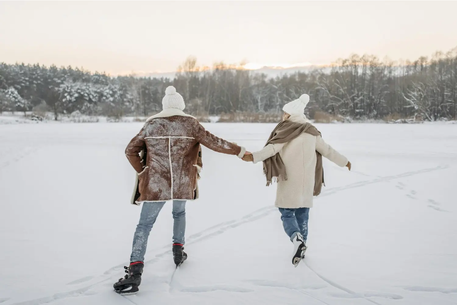 Zwei Personen in Winterkleidung laufen Hand in Hand auf einem zugefrorenen See im verschneiten Wald
