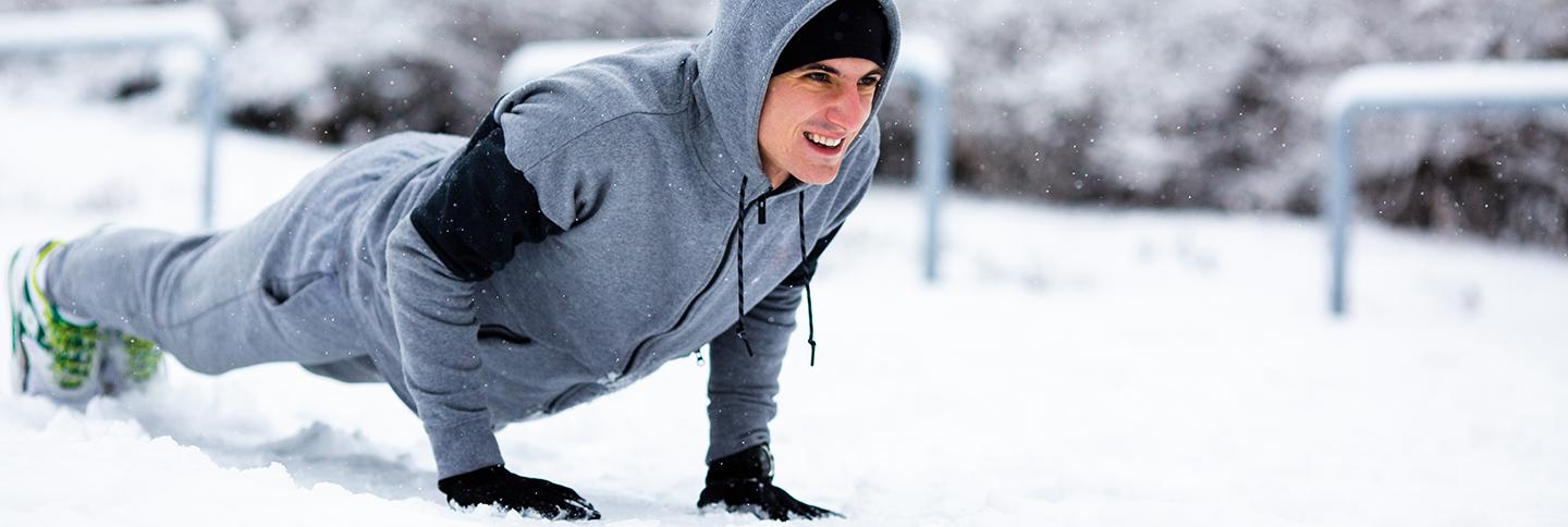 Junger Mann im grauen Trainingsanzug macht Push-ups im Schnee.