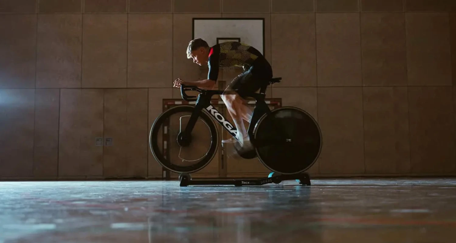 Radprofi trainiert auf einem Tacx-Rollentrainer auf einem KOGA-Zeitfahrrad in einer dunklen Sporthalle