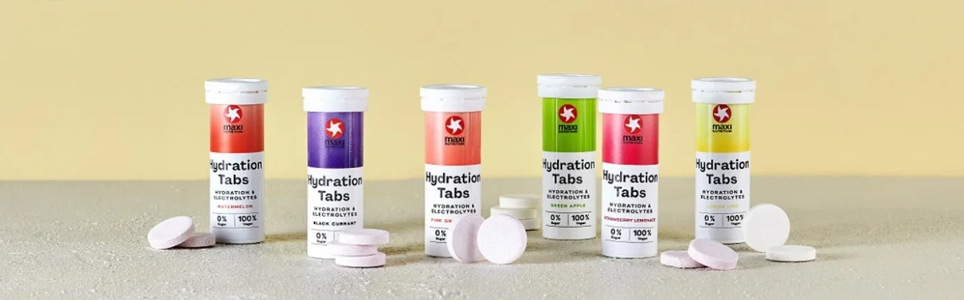 Sechs MaxiNutrition Hydration Tabs Röhrchen in allen Sorten nebeneinander mit losen Brausetabletten davor