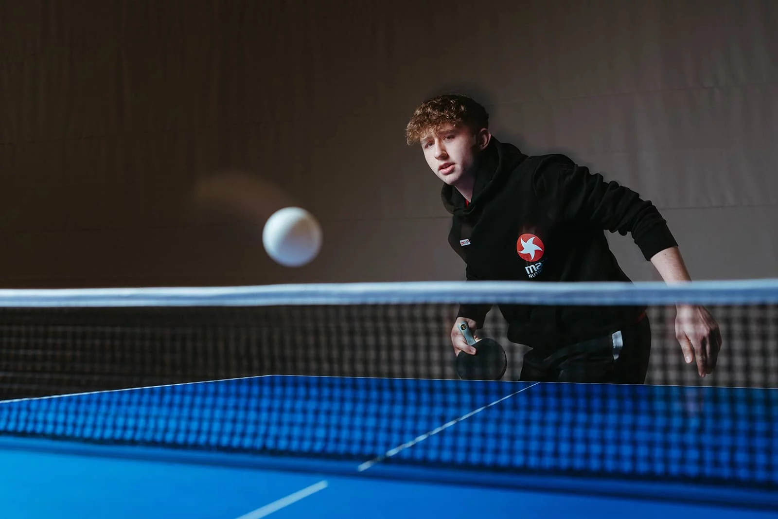 Julian Rzihauschek im MaxiNutrition-Hoodie konzentriert beim Tischtennisspielen